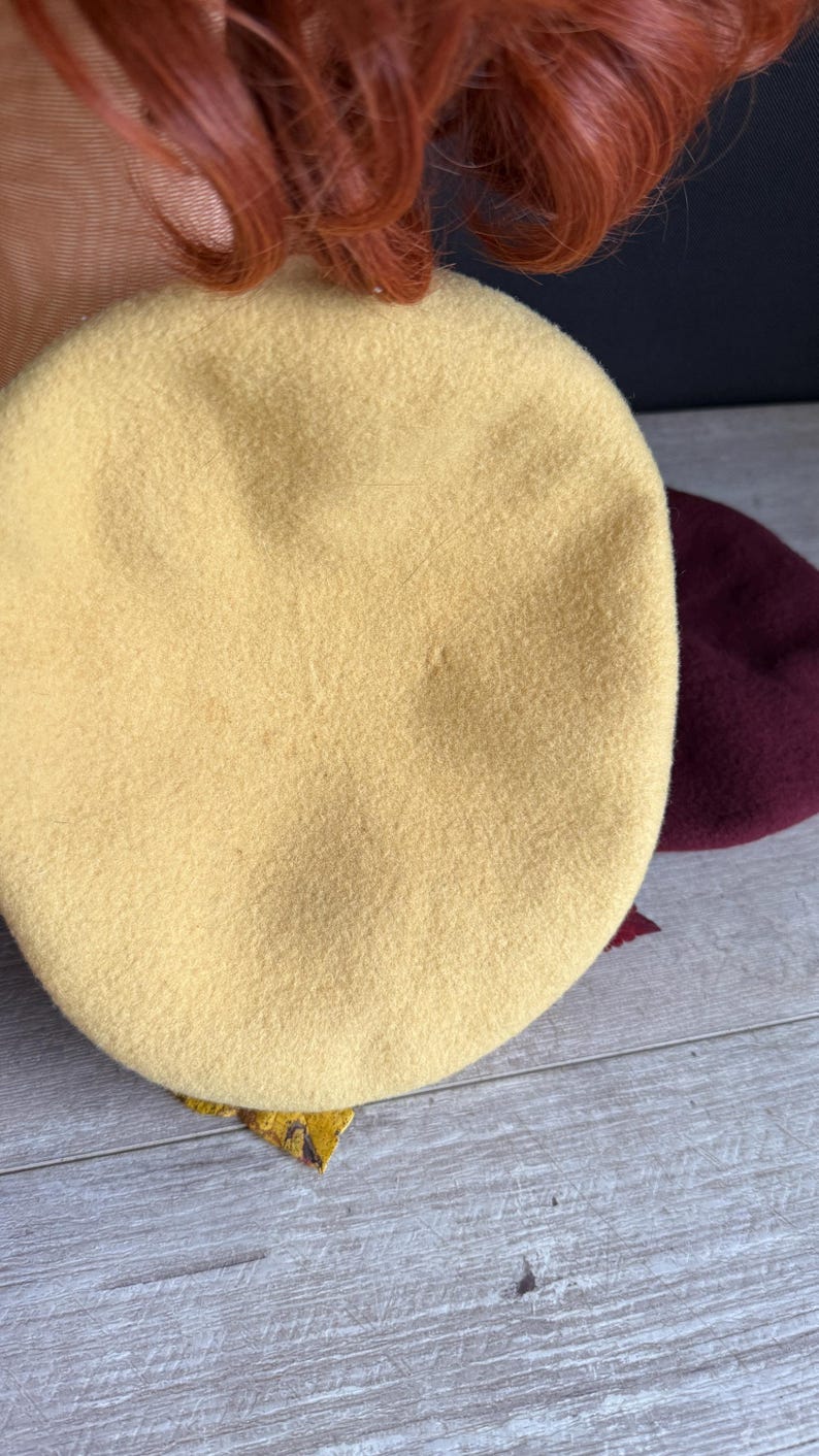 Puede incluir: Primer plano de dos boinas. La boina delantera es de color amarillo claro, mientras que la segunda es de color burdeos oscuro. Los sombreros est&aacute;n hechos de un material suave similar al fieltro, ideal para oto&ntilde;o o invierno.