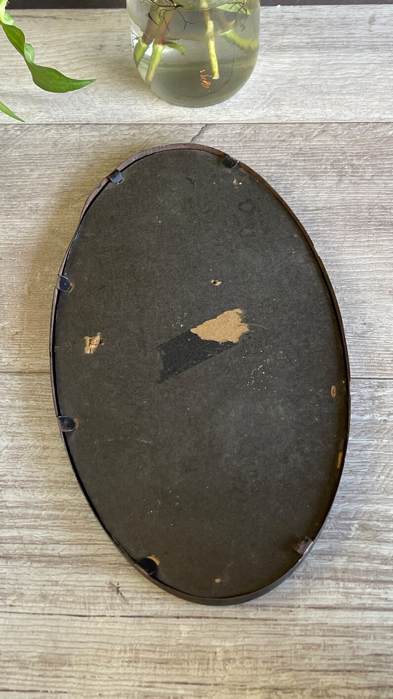 May include: A black oval picture frame with a dark brown mat. The frame has a slight curve to it and is made of wood.