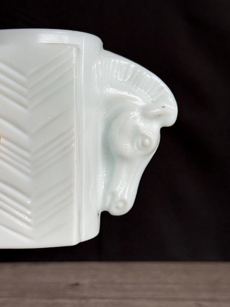 May include: A white, art deco style ceramic mug with a horse head design on the handle. The mug features a geometric pattern on the side and is set against a dark background.