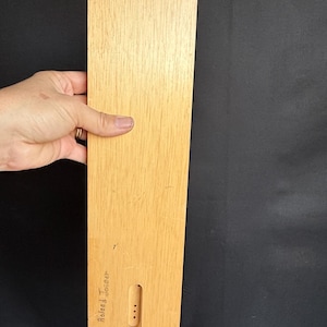 May include: A light-colored wooden ruler with a green sticker on the top right corner. The ruler has a rectangular shape with a cutout near the bottom. The text "Roland Joinder" is visible on the ruler.