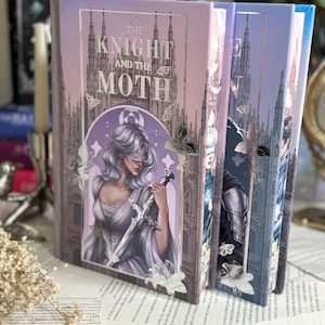Op de afbeelding: Een hardcover boek getiteld The Knight and the Moth met een lavendelkleurige en paarse kaft met een geblinddoekte figuur die een zwaard vasthoudt, omringd door motillustraties en een gotisch kathedraalsilhouet in goudfolie.