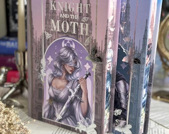 Puede incluir: Un libro de tapa dura titulado The Knight and the Moth con una cubierta lavanda y morada que muestra una figura con los ojos vendados sosteniendo una espada, rodeada de ilustraciones de polillas y una catedral gótica en lámina de oro.