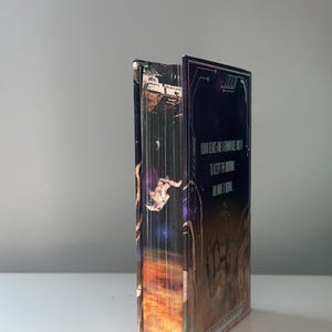Puede incluir: Un libro de tapa dura con una portada de tem&aacute;tica espacial. La portada presenta un astronauta, una nebulosa y el texto "HUMAN GENES HAVE A REMARKABLE HOLD TO KEEP THE UNIVERSE ALL WIDE & ETERNAL". El lomo del libro es visible.