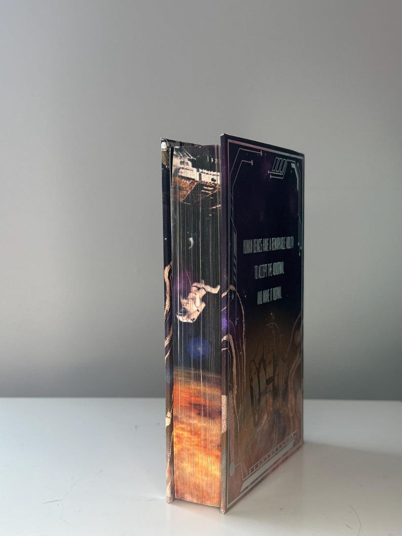 Puede incluir: Un libro de tapa dura con una portada de tem&aacute;tica espacial. La portada presenta un astronauta, una nebulosa y el texto "HUMAN GENES HAVE A REMARKABLE HOLD TO KEEP THE UNIVERSE ALL WIDE & ETERNAL". El lomo del libro es visible.