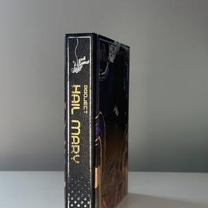Puede incluir: Un libro de tapa dura titulado "Project Hail Mary" de Andy Weir. El lomo es negro con letras doradas y un gr&aacute;fico de astronauta. La portada presenta una ilustraci&oacute;n de tem&aacute;tica espacial con fondo azul oscuro.