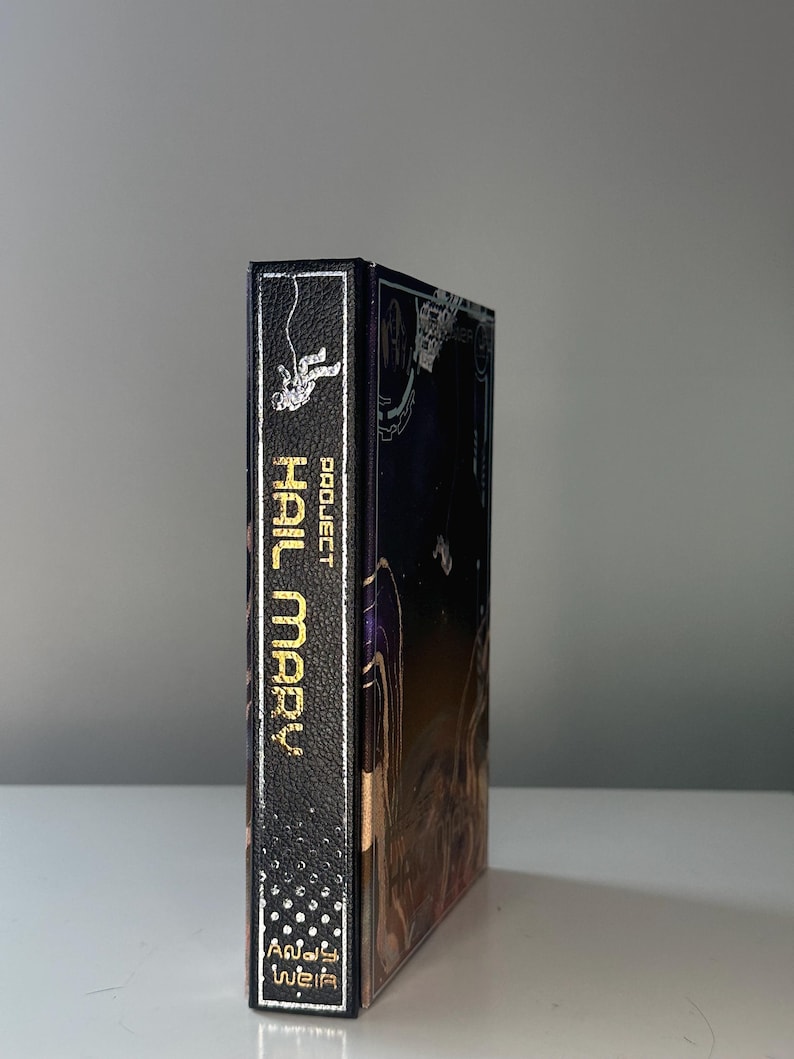 Puede incluir: Un libro de tapa dura titulado "Project Hail Mary" de Andy Weir. El lomo es negro con letras doradas y un gr&aacute;fico de astronauta. La portada presenta una ilustraci&oacute;n de tem&aacute;tica espacial con fondo azul oscuro.