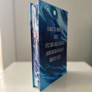 Pode incluir: Um livro de capa dura com uma capa azul e branca com o texto "ID MADE THE VAMPIRE GREAT, I FELT LIKE A REAL SUPERHERO, HARRY DRESDEN BREWS OF MONSTERS HEARTS". A lombada mostra uma m&atilde;o segurando uma bengala.