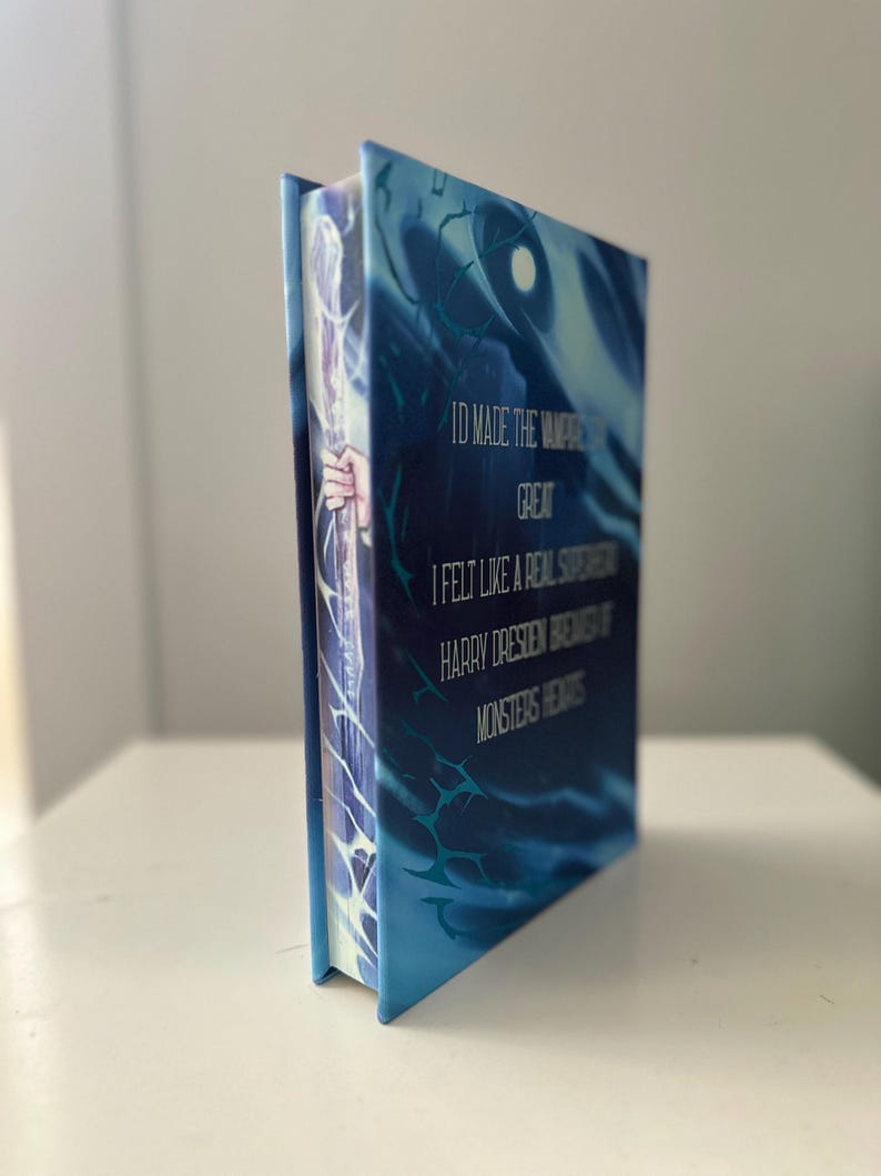 Pode incluir: Um livro de capa dura com uma capa azul e branca com o texto "ID MADE THE VAMPIRE GREAT, I FELT LIKE A REAL SUPERHERO, HARRY DRESDEN BREWS OF MONSTERS HEARTS". A lombada mostra uma m&atilde;o segurando uma bengala.