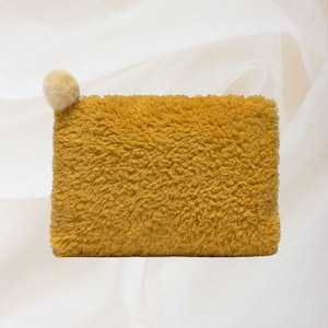 Puede incluir: Una bolsa amarilla peluda con un pequeño pompón blanco en la parte superior.