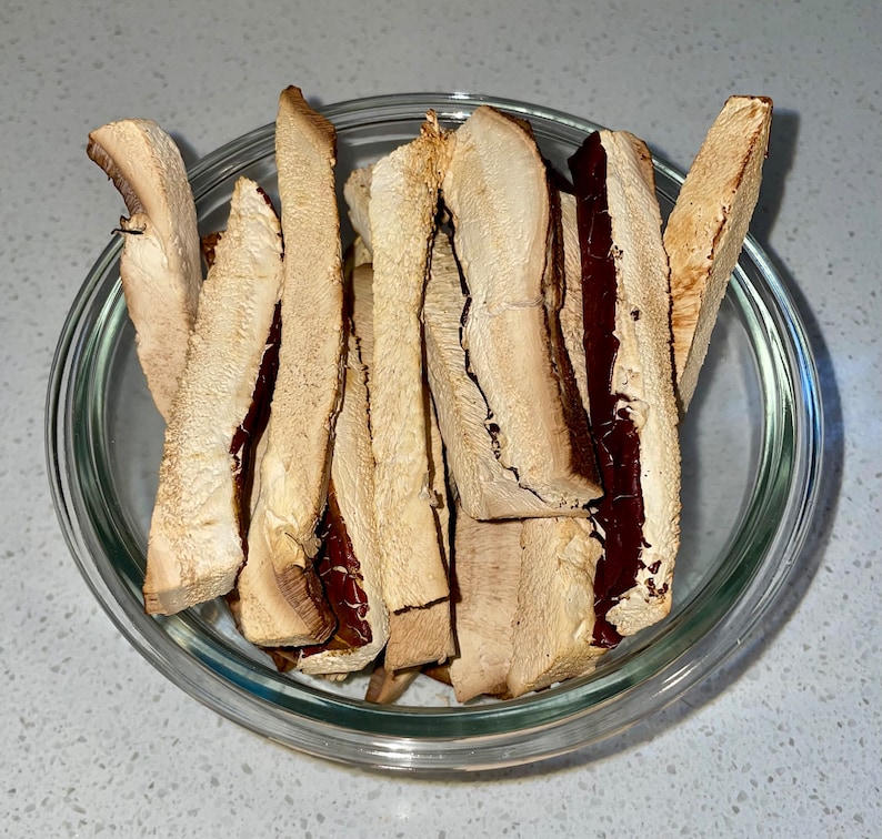 Op de afbeelding: Een glazen kom gevuld met gedroogde champignonschijfjes. De champignonschijfjes zijn lichtbruin met een roodbruine onderkant.