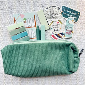 May include: A green corduroy pencil case with a zipper closure. The pencil case is filled with various stationery items, including pens, pencils, and sticky notes. There are also several stickers on the case, including one that says "Just one more chapter" and another that says "I read past my bedtime".