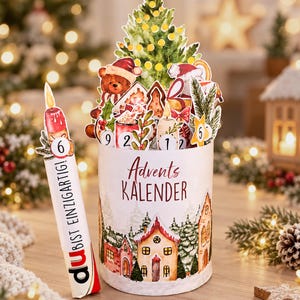 Può includere: Un calendario dell'Avvento cilindrico con un'illustrazione di un villaggio invernale e il testo Advents KALENDER. Un inserto a forma di candela mostra il numero 6 e il testo DU BIST EINZIGARTIG. La parte superiore presenta ritagli ad acquerello di un albero di Natale, un orsacchiotto e icone numerate.
