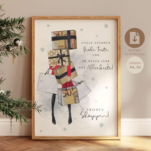 May include: A framed print featuring a watercolor illustration of a person carrying shopping bags and gift boxes. The print includes German text and snowflake accents. The boxes have "50 EURO" printed on them. The print is in a wooden frame.