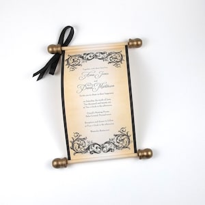 May include: A scroll wedding invitation on aged parchment paper with black text and ornate black filigree borders. The scroll is attached to two light-colored wooden rods with gold-toned finials and a black satin ribbon tied to the top left.