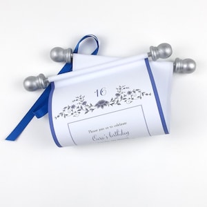 May include: A white scroll invitation with a blue border and accents, featuring a floral design and the number 16. The scroll is held by silver-colored rods and tied with a blue ribbon. The text reads "Please join us to celebrate Ciera's birthday."