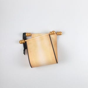 May include: A beige parchment scroll with a gradient finish, featuring dark brown edges and a black ribbon tie. The scroll is attached to two light-coloured wooden rods with rounded, metallic gold-coloured finials at each end of the rods.