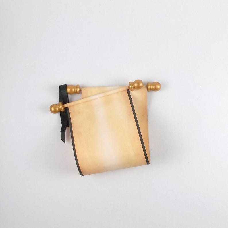 May include: A beige parchment scroll with a gradient finish, featuring dark brown edges and a black ribbon tie. The scroll is attached to two light-coloured wooden rods with rounded, metallic gold-coloured finials at each end of the rods.