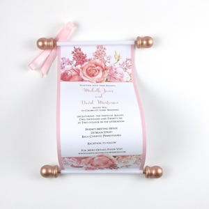 May include: A wedding invitation scroll with a floral design in pink and peach tones. The invitation includes the names Michelle Jones and David Martinson, along with the wedding date and location. The scroll is held by rose gold-colored end pieces and a pink ribbon.