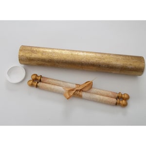May include: A gold-colored scroll case with a matching lid and two rolled scrolls tied with a gold ribbon. The scrolls have gold finials and a cream-colored paper with a subtle floral pattern. The case has a textured finish.