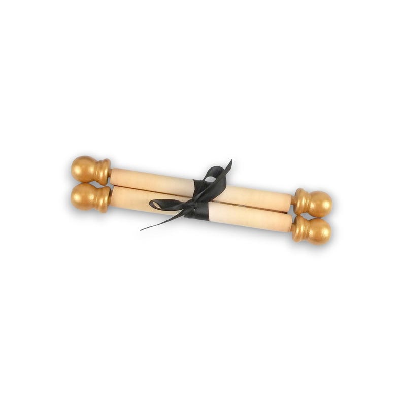 May include: A rolled parchment scroll featuring light beige paper, secured in the centre with a black satin ribbon tied in a bow. The ends of the scroll are capped with smooth, spherical gold-coloured finials on both sides of the cylinder.