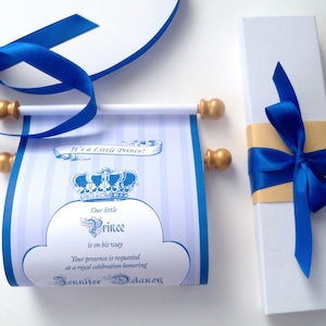 May include: A blue and gold scroll invitation with the text "It's a Little Prince!" and "Our little Prince is on his way." The scroll is tied with a blue ribbon and comes in a white box with a blue ribbon.