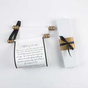 May include: White scroll with gold accents and black ribbon. The scroll is unrolled, revealing handwritten text. A matching white box with a gold band and black ribbon is also present. The text reads "My dearest Emily".