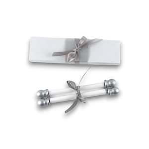 May include: A rectangular white gift box wrapped with a silver ribbon and a pair of white taper candles with silver ball-shaped finials at each end, tied together with a matching silver ribbon, presented as a set for decorative use.