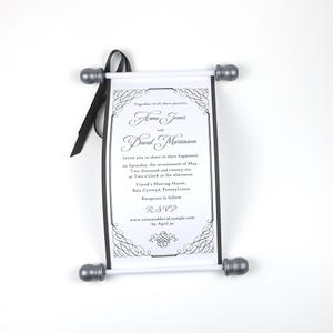 May include: A wedding invitation scroll with a black ribbon and silver-colored end caps. The invitation features the names Anna Jones and David Martinson, along with event details. The scroll is white with black text and decorative borders.