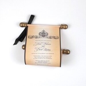 May include: A wedding invitation scroll with gold-colored finials and a black ribbon. The invitation features ornate scrollwork and the names "Anna Patterson and David Landry". The text invites guests to celebrate the wedding on June 10, 2026.