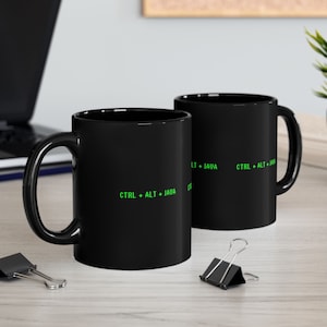 May include: Two black coffee mugs with a green text design that reads "CTRL + ALT + JAVA".