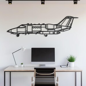 May include: Black metal jet airplane wall art. The decorative piece is mounted on a white wall above a desk. The jet has a detailed outline with visible wings, tail, and cockpit. The artwork adds a modern touch to the room.