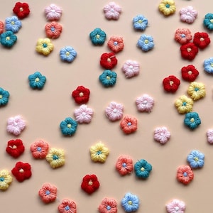 May include: Assortment of colourful embroidered flower patches in various shades of pink, red, blue, green, yellow, and orange. The patches are scattered on a light beige background.