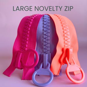 May include: Three large novelty zippers in fuchsia, lavender, and coral. Each zipper has a matching pull tab. The text "LARGE NOVELTY ZIP" is at the top. These zippers are suitable for craft projects and are available in various sizes.