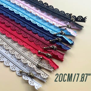 May include: Assortment of 10 different colours of 20 cm zipper tape with a delicate lace trim. The zippers have a bronze pull with a chain.