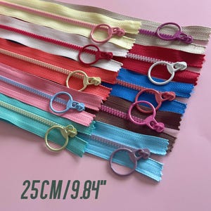 以下が含まれることがあります： プラスチックのスライダー付きのカラフルなジッパーテープの詰め合わせ。ジッパーテープは扇形に配置されており、長さは25cm/9.84インチです。