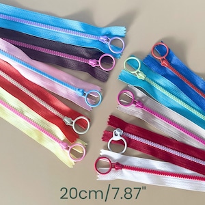 May include: A selection of colourful zippers in shades of blue, pink, red, and white. Each zipper has a ring pull and measures 20cm (7.87 inches) in length. The zippers are arranged in a fan-like pattern.
