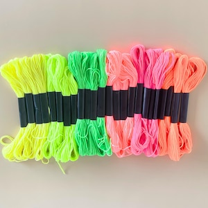 May include: A selection of neon embroidery floss in yellow, green, pink, and orange. Each bundle is held together with a black band. These bright threads are ideal for embroidery and other craft activities.