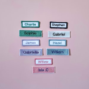 May include: A collection of rectangular embroidered name patches in various colours including green, white, purple, blue, and pink. Each patch features a unique name stitched in a contrasting thread colour, including Charlie, Sophie, James, Gabriella, Stephen, Gabriel, Hazel, William, Willow, and Isla .C.
