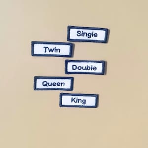 May include: Five rectangular embroidered patches with white centers and dark blue borders. Each patch features black text reading Single, Twin, Double, Queen, or King. The patches are arranged in a staggered vertical column against a solid background.
