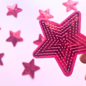 May include: Pink sparkly star-shaped fabric patches. The stars are made of sequins and have a pink felt backing.