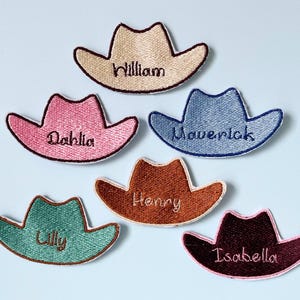May include: Six embroidered cowboy hat patches in various colours including beige, pink, blue, brown, teal, and dark maroon. Each patch features a custom name stitched in the centre: William, Dahlia, Maverick, Henry, Lilly, and Isabella.