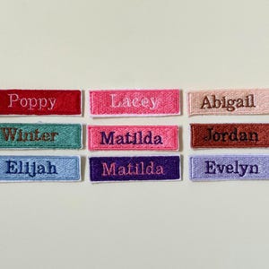 May include: A selection of embroidered name patches in shades like red, pink, teal, and purple. Each patch displays a different name in a contrasting colour, including "Poppy," "Lacey," and "Abigail."