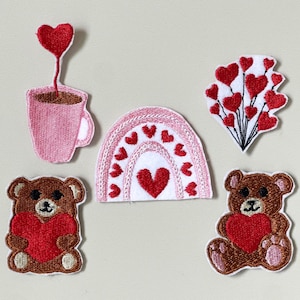 May include: A selection of embroidered patches with Valentine's Day motifs. The designs include a pink coffee cup with a heart, a rainbow with hearts, a bouquet of hearts, and two teddy bears holding hearts. The patches are in pink, red, and brown.