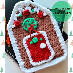 May include: A crocheted e-reader sleeve shaped like a gingerbread house. The brown sleeve features white frosting trim, red and green decorations, and a red door. The text "GINGERBREAD HOUSE EREADER SLEEVE Crochet Pattern" is displayed.