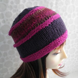 May include: A purple and pink knit hat with a striped pattern. The hat is made with a soft yarn and has a comfortable fit.