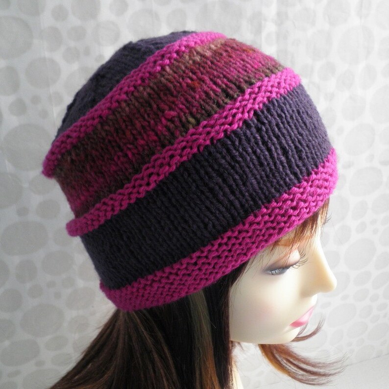 May include: A purple and pink knit hat with a striped pattern. The hat is made with a soft yarn and has a comfortable fit.