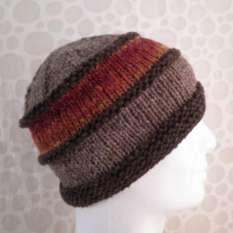 May include: A brown knit hat with a wide orange, red, and yellow stripe. The hat has a dark brown brim.