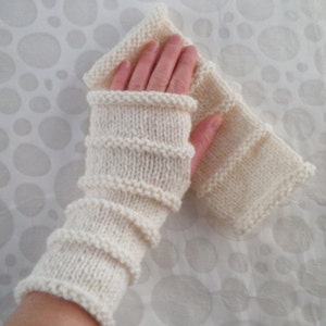 May include: White knitted fingerless gloves with a ribbed pattern. The gloves are folded over and show the inside of the knit.