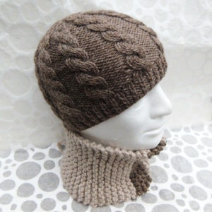 May include: A brown knit hat with a cable knit design and a matching tan knit cowl. The hat is a dark brown color and the cowl is a lighter tan color. The hat and cowl are displayed on a white mannequin head.