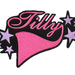 Könnte beinhalten: Rosa-schwarzer gestickter Aufnäher mit dem Wort "Tilly" in kursivschrift und fünf lila Sternen.
